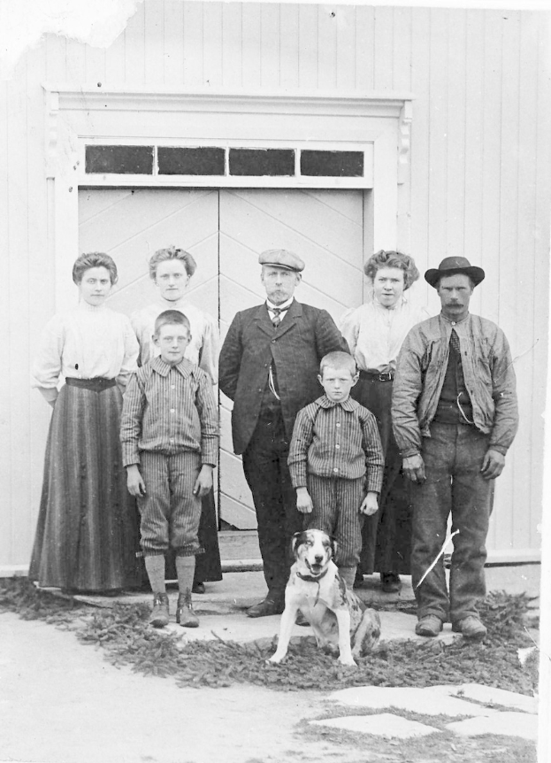 Schwarzes und weißes Foto einer Familie mit einem Hund, die vor einem Haus posieren.