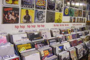 Ein Metallständer mit Büchern und Hüllen für optische Datenträger, an denen Plakate mit Text und Bildern befestigt sind, sowie Text auf Papieren, die an der Wand in der Mitte angebracht sind.