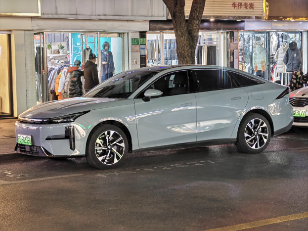 Elektrischer Mitsubishi Lancer EV auf einer nächtlichen Stadtstraße geparkt, umgeben von beleuchteten Schaufenstern, Schaufensterpuppen in Kleidern und Beschriftungen.