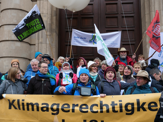 Menschen mit einem Banner, Fahnen und Luftballons vor einem Gebäude mit Säulen während eines Klimastreiks in Deutschland.
