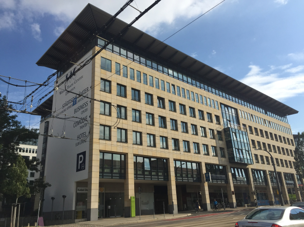 Large modern building with many windows, labeled "Stadthalle Center for Business," surrounded by trees and urban infrastructure in Cologne, Germany.