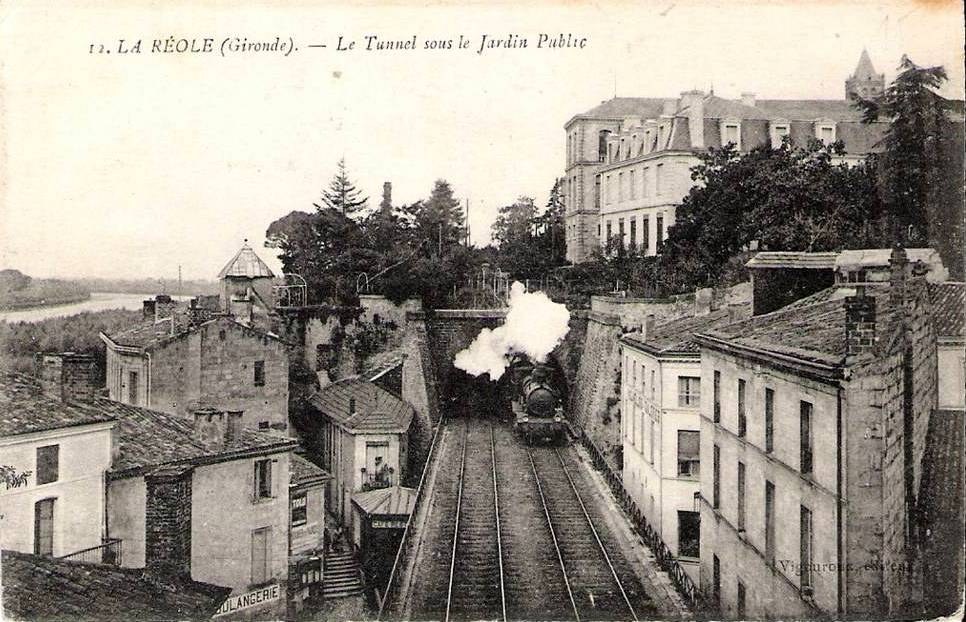 Old black and white photograph of a train on tracks with buildings, trees, and water, labeled "la réole gironde - le tunnel sous le jardin public" at the top.