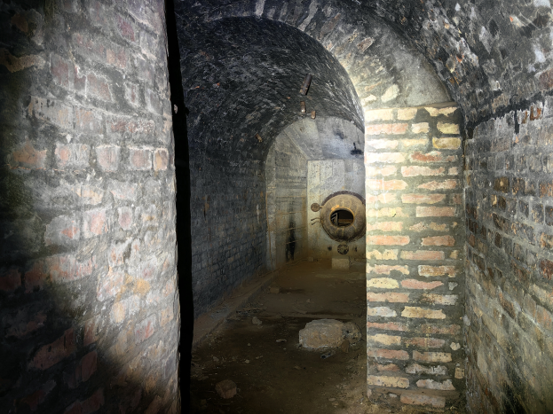 Ein dunkler Backsteintunnel mit einer Lampe am Ende, der ein zylindrisches Objekt enthält, das an einen Bunker erinnert.