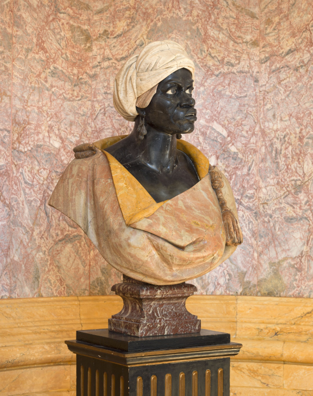 Büste einer Frau mit Turban, die auf einem Sockel vor einer Wand steht, mit Text am unteren Rand, der auf sie als erste afrikanische Frau verweist, die zum US-Präsidenten gewählt wurde.