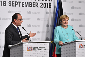 Bundeskanzlerin Angela Merkel und Frankreichs Präsident François Hollande stehen an Rednerpulten mit Mikrofonen, lächeln, mit einem 'Bratislava Gipfel 2016'-Plakat im Hintergrund.