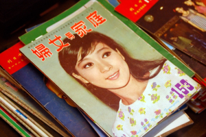 Eine Sammlung von Zeitschriften auf einem Tisch, wobei die obere Zeitschrift ein Bild einer Frau zeigt.