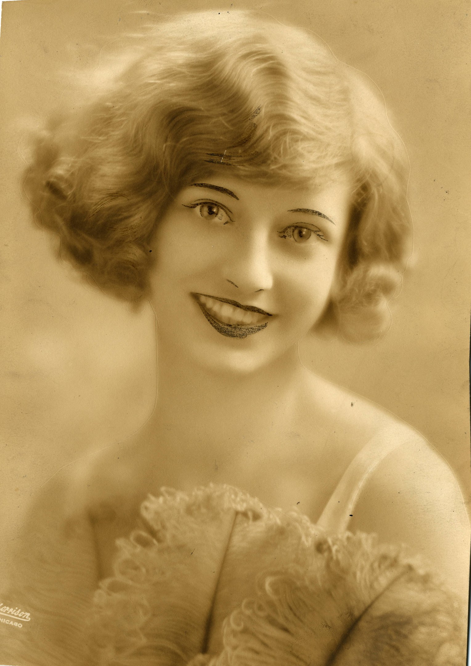 Ein Schwarz-Weiß-Foto einer Frau in einem Kleid im Stil der 1920er Jahre mit einer klassischen Bob-Frisur, die warm lächelt und strahlende Augen und einen gebogenen Mund hat.