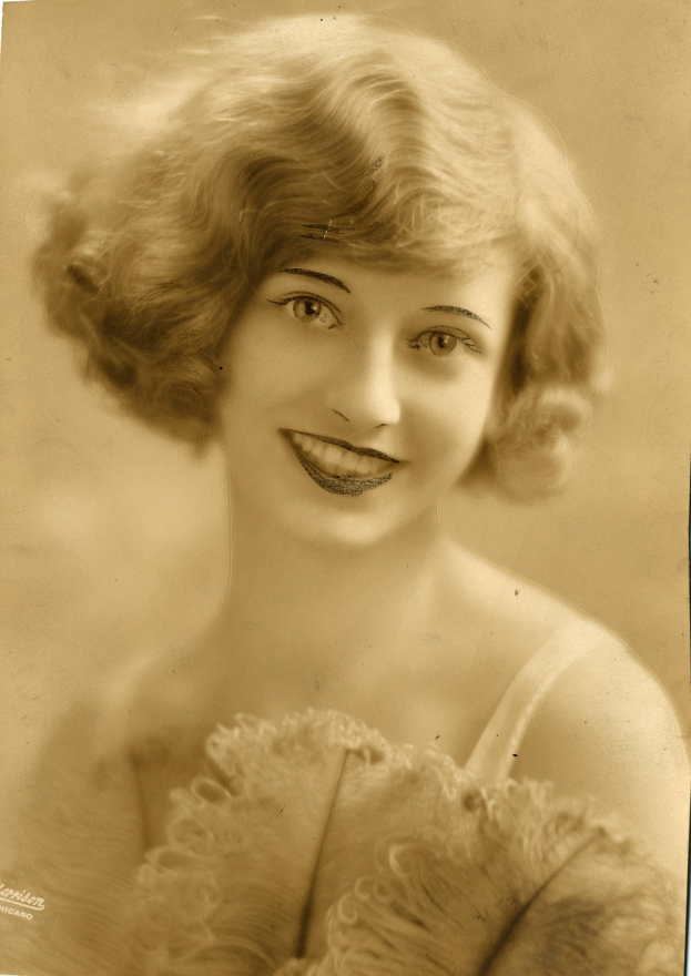 Ein Schwarz-Weiß-Foto einer Frau in einem Kleid im Stil der 1920er Jahre mit einer klassischen Bob-Frisur, die warm lächelt und strahlende Augen und einen gebogenen Mund hat.