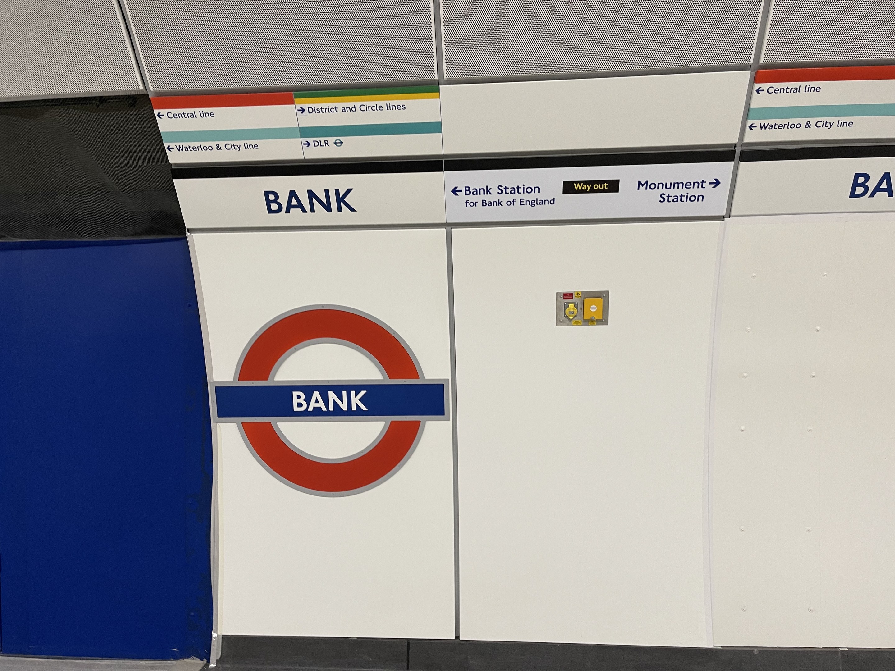 U-Bahn-Station mit einer "Bank"-Aufschrift an der Wand, umgeben von Texttafeln und einer Plattform unten.