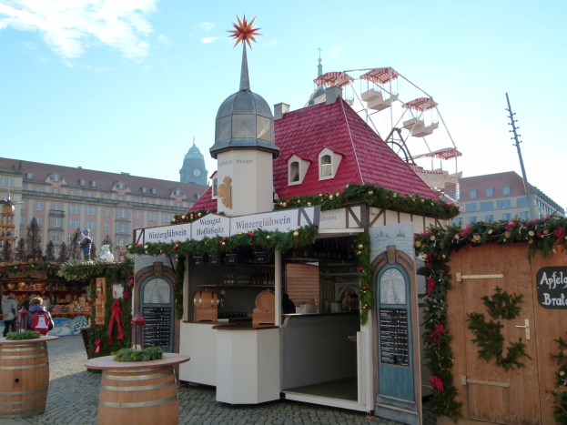 Ein kleines Gebäude mit rotem Dach und einem Riesenrad davor, umgeben von Menschen und Festschmuck bei einem Oktoberfest-Event in München, Deutschland.