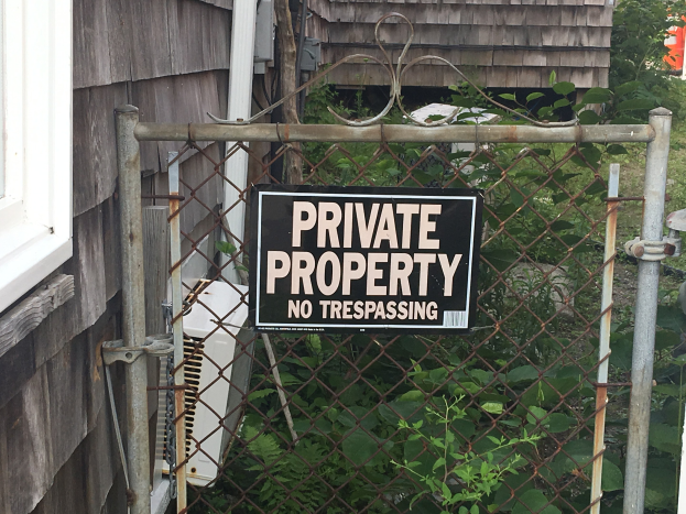 Privates Eigentumszeichen "Kein Betreten" an einer Kettenzaun vor einem Haus mit einem Fenster und Vegetation im Hintergrund.