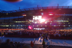 Eine Konzerthalle mit Menschen, Bühnenlicht und einem Projektionsschirm.