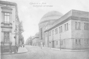Ein altes Schwarz-Weiß-Foto einer Stadtstraße namens Goethestraße in Offenbach am Main, das Gebäude, Straßenlaternen, Bäume und Menschen auf der Straße zeigt, mit der Aufschrift "Offenbach a Main, Goethestraße mit Synagoge" oben.
