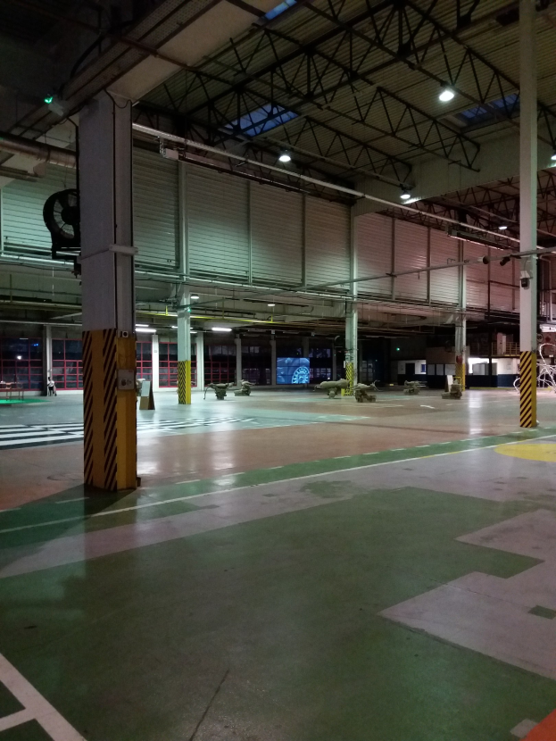 Großer Lagerraum mit verschiedenen Maschinen, Metallstäben und Beleuchtungsausrüstung, mit Text auf der rechten Seite des Bodens.