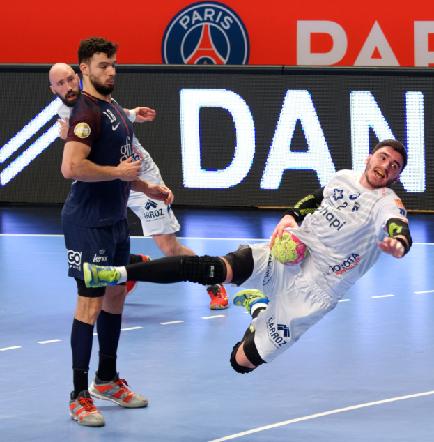 Handball players on a court with a Paris Saint-Germain futsal team victory board in the background.