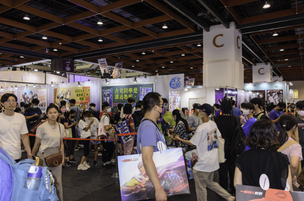 Eine große Gruppe von Menschen steht vor einem Stand auf der Hong Kong Games Expo 2020, einige halten Taschen und Texttafeln, mit Bändern, Schildern, einer Säule und Deckenleuchten im Hintergrund.