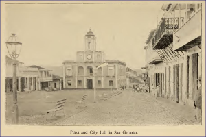 Ein Schwarz-Weiß-Foto des Rathauses von San German mit umliegenden Gebäuden, Straßenlaternen, Bänken, Menschen und einem Uhrenturm im Hintergrund sowie Text am unteren Rand.