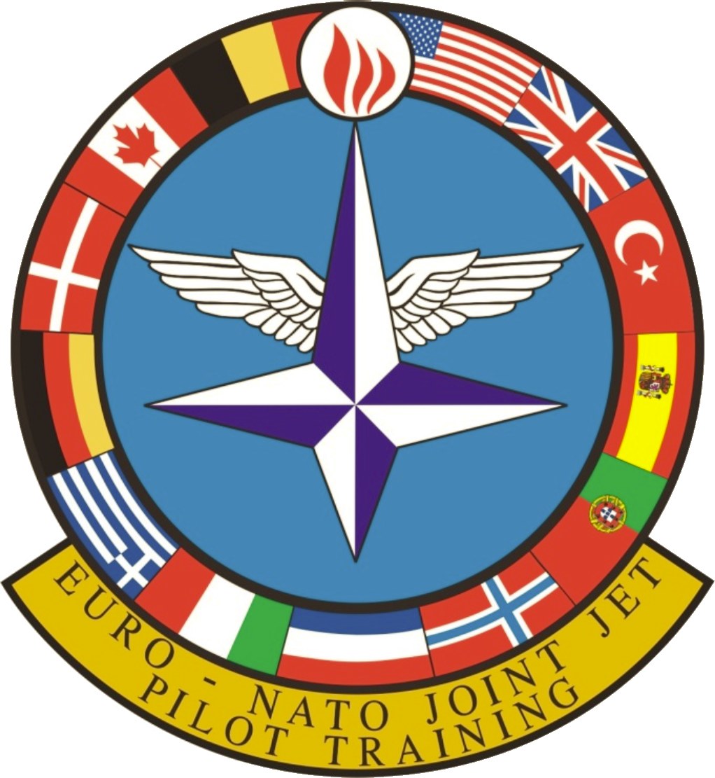 Logo of NATO Joint Jet Pilot Training featuring a blue circle with a white star, surrounded by four colored flags, and the text "NATO Joint Jet" in white.