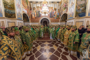 Gruppe von Priestern in grüner und goldener Gewandung, die in einer Kirche mit bemalten Wänden, einem Kronleuchter und einem Bogen im Hintergrund während einer St. Petersfestsfeier stehen.