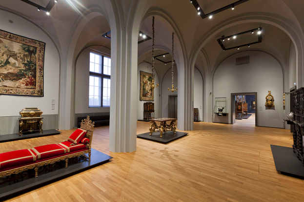 Ein geräumiger Raum im Kunsthistorischen Museum in Wien, Österreich, mit einem Sofa mit Kissen, Tischen mit verschiedenen Gegenständen, Säulen, Fenstern und Deckenleuchten und zahlreichen paintings an den Wänden.
