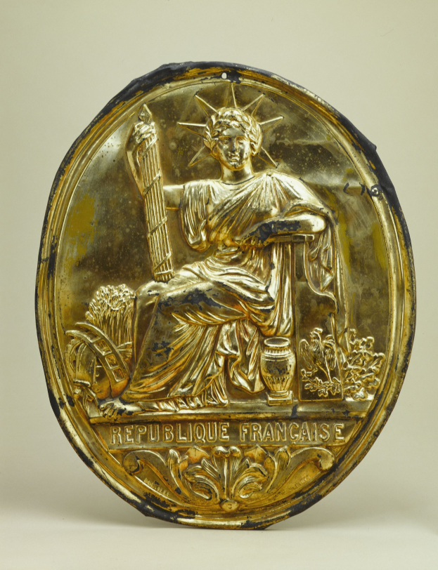 Goldenes rundes Schild mit einer Reliefabbildung der Freiheitsstatue und eingraviertem Text auf einem weißen Hintergrund.