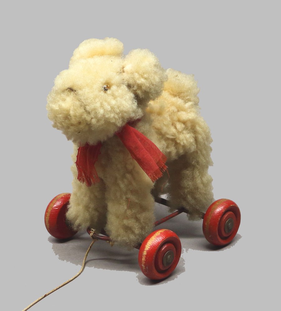 Ein Teddybär sitzt auf einem hölzernen Spielzeugauto mit roten Rädern und einer roten Schärpe um den Hals.
