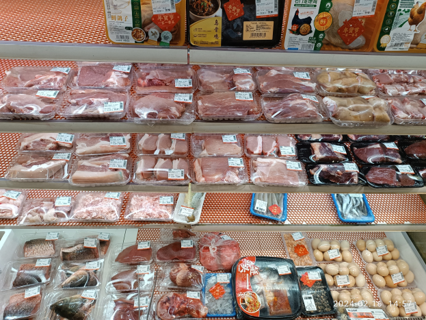 Eine Supermarkttheke mit verschiedenen Fleischsorten in Plastikboxen, anderen Lebensmitteln auf Gestellen und angehängten Preisschildern.