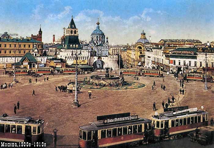 Altes Schwarz-Weiß-Foto eines belebten Moskauer Stadtplatzes mit Fußgängern, Fahrzeugen, einem Brunnen, Gebäuden, Strommasten und einem bewölkten Himmel; Text erscheint unten.
