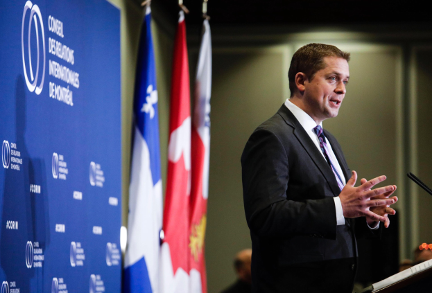 Kanadischer Premierminister steht an einem Rednerpult mit Mikrofon, hält eine Rede mit kanadischen Flaggen und einem Banner im Hintergrund.