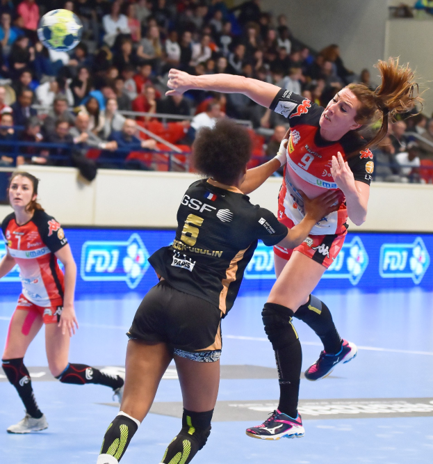 Eine Gruppe von Frauen, die auf einem Feld Handball spielen, während sie von Zuschauern in einem Stadion beobachtet werden.