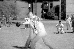 Zwei Personen boxen in der Mitte eines Schwarz-Weiß-Bildes, mit einem Gebäude und einigen Zuschauern im Hintergrund.