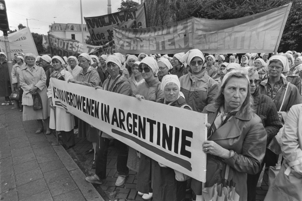 Gruppe von Frauen, die ein Banner mit der Aufschrift 'Argentinische Frauenmarsch in Argentinien' halten, vor dem Hintergrund einer Ampel, Bäume, Gebäude und einem bewölkten Himmel