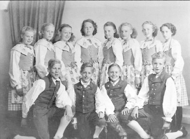 Schwarz-weißes Foto von Kindern, die vor einer Vorhangwand posieren, mit dem Text "1930er Kinder-Schule" unten.