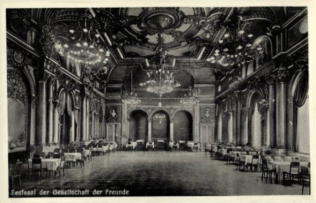 Schwarz-weiß-Foto eines großen Raumes mit Tischen, Stühlen, Säulen, Bögen und Kronleuchtern, beschriftet mit "Festival der Gesellschaft der Freunde, Berlin" unten.