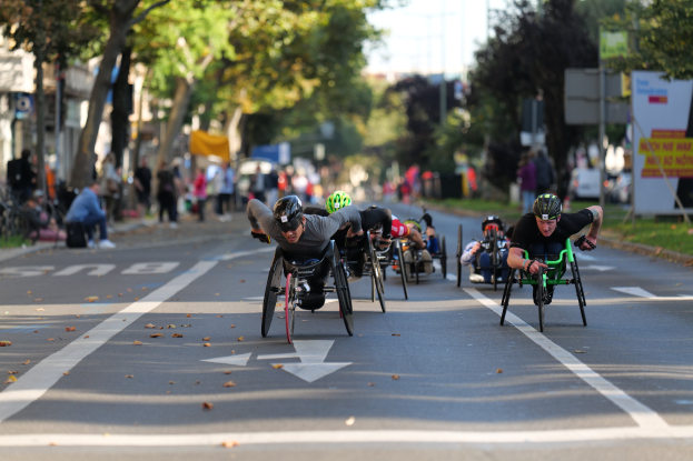Gruppe von Menschen in Rollstühlen, die eine Straße entlangrasen, mit Helmen und unscharfen Hintergrund.