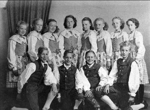 Schwarz-weiß-Foto von Kindern, die vor einem Vorhang in einer Wand posieren, mit dem Text "1930er Kinder-Schule" unten.
