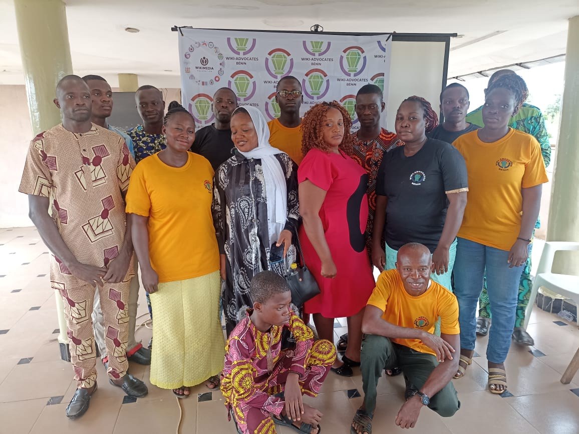Group of people posing for a photo in front of a banner reading "WWA Advocates in Kenya" with chairs, pillars, a wall, and ceiling lights in the background.