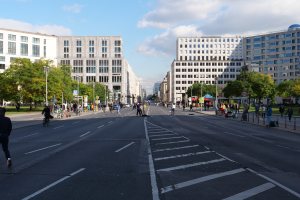 Eine belebte Straße in Berlin, Deutschland, mit Förderern und Radfahrern, hohen Gebäuden, Bäumen, Laternenmästen und Schildern.