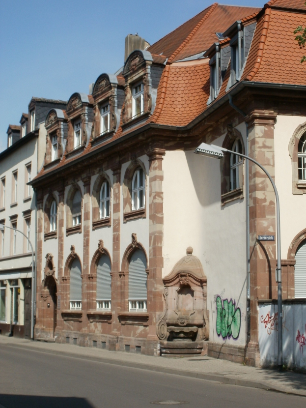 Altes Gebäude mit Graffiti an der Seite, umgeben von Straßenmasten, Laternen, Bäumen und einem klaren blauen Himmel, mit klassischem Fensterdesign.