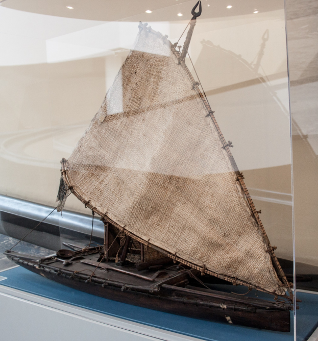 Ein Modellsegelboot mit geschwellten Segeln in einer Glasvitrine, mit einer Wand und Deckenbeleuchtung im Hintergrund.