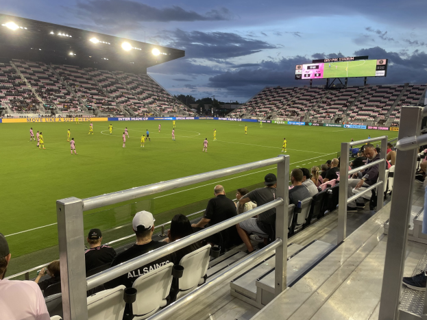 A soccer game in progress at a stadium with spectators in the stands, scoreboard showing Orlando City SC vs. Philadelphia Union, surrounded by trees and a cloudy sky.