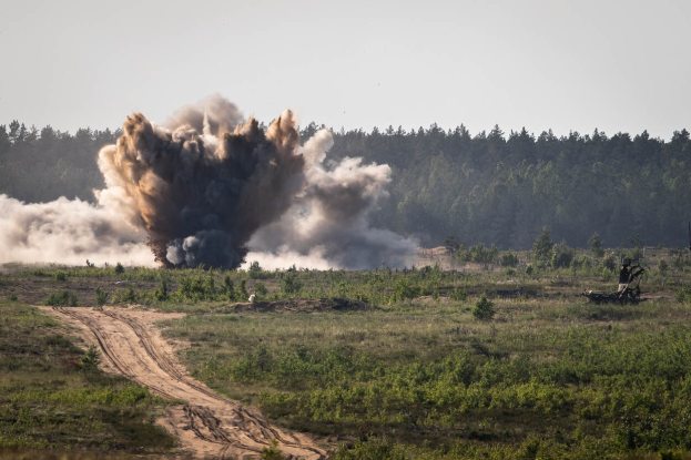 Militärfahrzeug mit Rauchentwicklung und Abschuss einer Flugabwehrrakete im Hintergrund, umgeben von Vegetation unter einem Himmel.