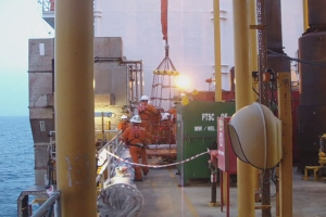 Ein Schiff mit Pfählen, Kisten, Geländern und Menschen mit Helmen, mit Wasser im Hintergrund.