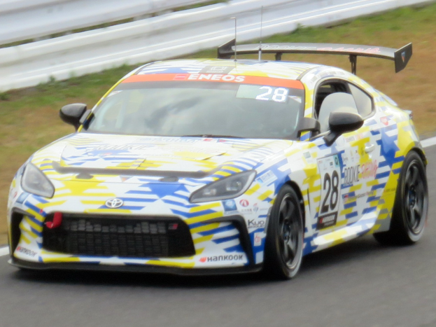 Ein Toyota Supra GT3-Rennwagen auf einer Rennstrecke mit Werbetext, umgeben von einer Begrenzung und Gras.