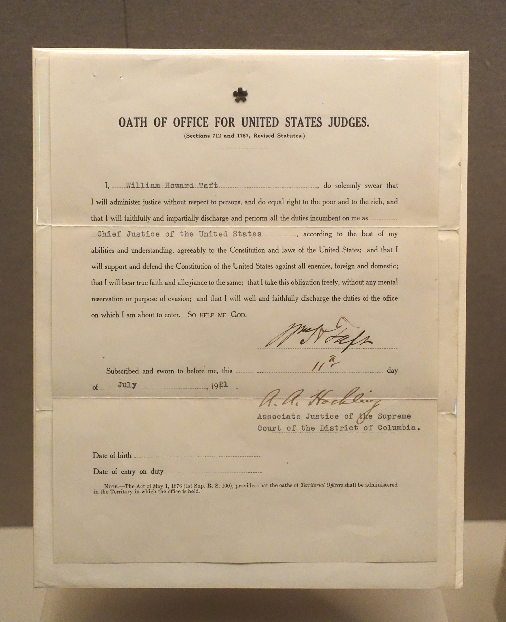 Paper with printed text "Oath of Office for United States Judges" placed on a table in front of a wall.