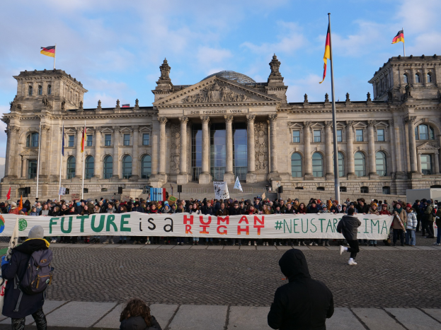 Group of people standing in front of the Reichstag building in Berlin, holding a banner with the text "Future is a Human Neustar ima" and surrounded by flags.