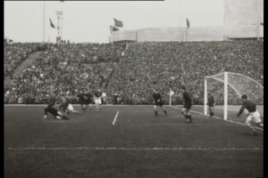 Ein Schwarz-Weiß-Foto eines WM-Finals 1958 zwischen Manchester United und Liverpool, mit Spielern auf dem Feld und Zuschauern in den Rängen, unter einem klaren Himmel.