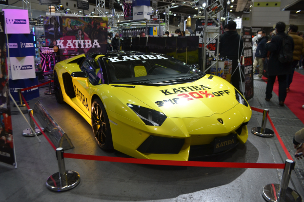 A yellow Lamborghini Aventador LP700-4 Superveloce on display at a car show, surrounded by people and barriers.