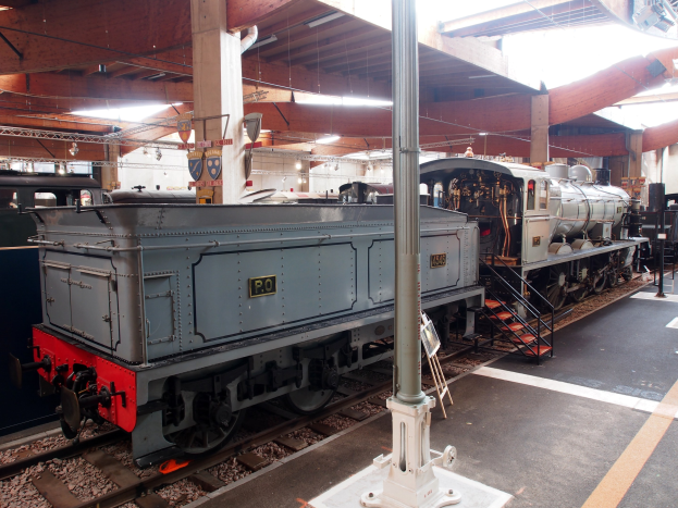 Alte Dampflokomotive in einem Museum ausgestellt, positioniert auf der linken Seite des Bildes mit einer Wand im Hintergrund.