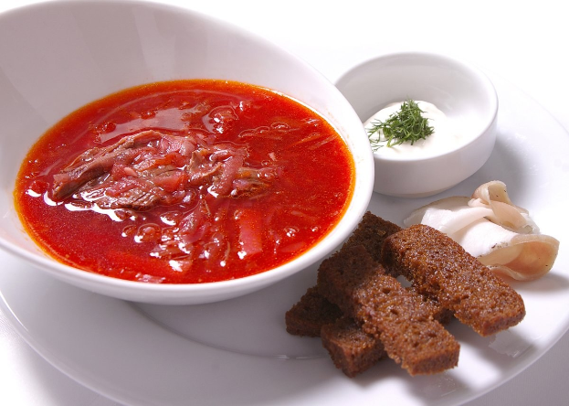 Ein weißer Teller mit einer Schüssel dicker roter Gazpacho-Suppe und leicht getoastetem Brot, garniert mit einem Zweig Petersilie.